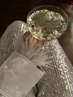 a person is holding a wine glass in their hand with some white feathers on it