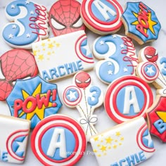 decorated cookies are arranged in the shape of superheros and stars, with numbers on them