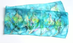 "Tulip blossoms art scarf in watercolor style. Ocean inspired colors: intense shades of warm blue and bright green with a hint of purple. Beautifully shines with gold outlines. Hand painted 100% silk with hand-rolled edges. Painted on Chiffon 6 pure silk. Chiffon 6 is similar to habotai or ponge 05 silk but it is thicker and produce wonderfully vivid colors. Doesn't wrinkle as much as habotai. Chiffon 6 is actually not a well known silk type despite its great qualities. The silk dyes are non-tox Artsy Blue Art For Collection, Elegant Hand Dyed Silk Scarf, Silk Tulips, Artistic Hand Dyed Blue Silk Scarf, Artistic Blue Silk Scarf, Artistic Hand-dyed Silk Scarves, Blue Hand-dyed Silk Scarf For Summer, Pure Silk Scarf, Fairy Decor