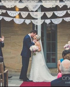 a bride and groom kissing in front of an outdoor wedding ceremony with white crochet hanging from the ceiling