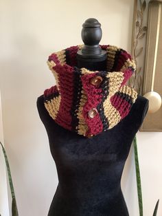 a black mannequin wearing a multicolored knitted cowl with buttons