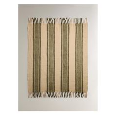 a beige and green striped rug with fringes on the bottom, in front of a white wall