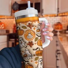 a woman holding up a cup with halloween decorations on it and pumpkins in the background