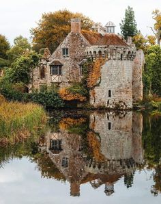 an old stone building sitting on top of a lake next to a lush green forest