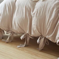 an unmade bed with beige linens and bows on the headboard, along with wooden flooring