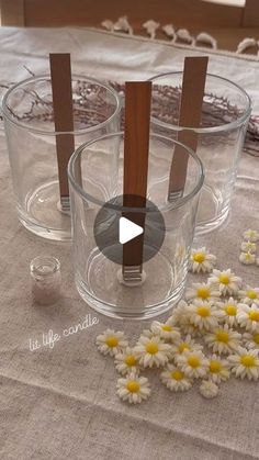 two clear cups with wooden sticks sticking out of them on a table cloth next to daisies