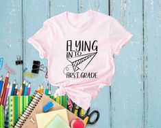 Get ready to soar into a new school year with our Flying Into First Grade Shirt! Perfect for your little one's first-grade adventures, this shirt is designed to celebrate this exciting milestone with style and fun. 🌟🎉 Comfortable Fabric: Made from soft, breathable material to keep your child comfy all day long. ☁️👕 Adorable Design: Features a cute airplane graphic with "Flying Into First Grade" text, making it a delightful choice for school days. ✈️❤️ Perfect Fit: Available in various sizes to ensure a great fit for your growing first-grader.  Versatile Wear: Ideal for the first day of school, picture day, or any school event. Pairs well with jeans, shorts, or skirts!  Great Gift: A wonderful gift for your child or any first-grader, making their new school year even more special. 🎁🎒 C Back To School Name Print Tops For College, Pink T-shirt For Back To School, Crew Neck Tops For End Of School Year Events, Name Print Tops For College Back To School, Graphic Tee For End Of School Year Events, End Of School Year Graphic Tee For School Events, Educational College T-shirt With Letter Print, Back To School Letter Print Tops For School Events, Pink Slogan T-shirt For School