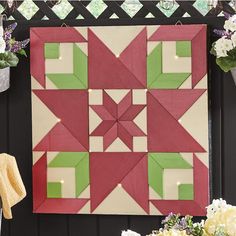 a red and green quilt hanging on the side of a black wall next to flowers