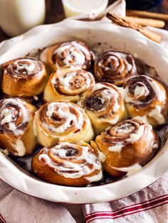 cinnamon rolls with icing in a white casserole dish on a red and white towel