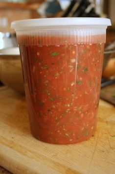 a plastic cup filled with salsa sitting on top of a wooden cutting board