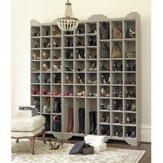 a room filled with lots of shoes on shelves next to a chair and ottoman in front of a chandelier