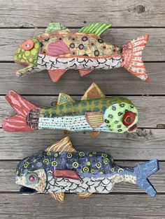 three decorative fish are sitting on a wooden surface, one is painted green and the other is red