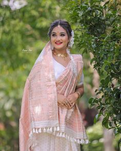 a woman wearing a pink and white sari standing in front of some green trees