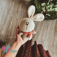 a person holding up a crocheted bunny doll in front of some carrots