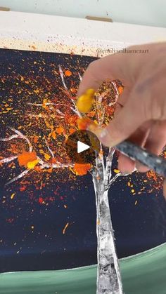 someone is painting a tree with oranges and yellows on the bottom half of it