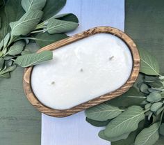 a white candle with green leaves around it on a blue and white table cloth next to some greenery