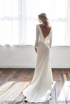 a woman standing in front of a window wearing a long white dress with beading on the back