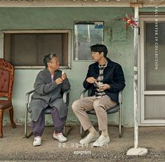 two men sitting on chairs in front of a building with an awning over them