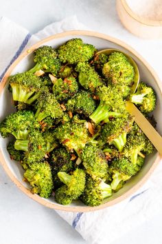 a bowl full of broccoli with a spoon in it next to a napkin