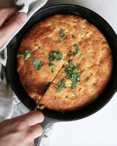 a person cutting into a cornbread with cilantro and parsley in a cast iron skillet