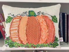 a decorative pumpkin pillow on a shelf with books in the backgroung behind it