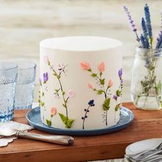 a white cake decorated with flowers on a blue plate next to silverware and glasses