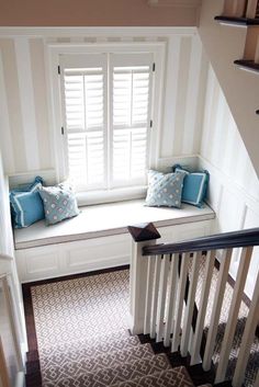 a window seat with two pillows on it in front of a white wall and stairs