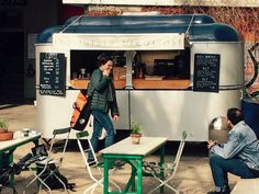 two people sitting at tables in front of a food truck