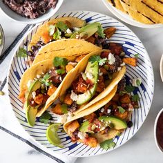 three tacos on a plate with salsa and tortillas