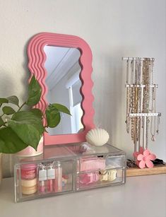 a pink mirror sitting on top of a table next to a potted plant and other items