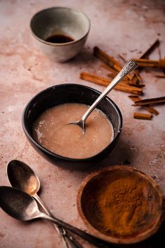 two bowls filled with liquid next to spoons and cinnamon sticks on a counter top