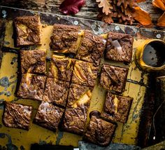 some brownies are sitting on a table next to a cup of coffee and autumn leaves