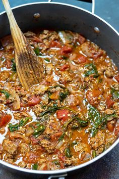 a pan filled with meat and vegetables on top of a table next to a wooden spoon