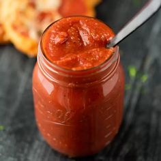 a jar filled with sauce sitting on top of a table next to a slice of pizza