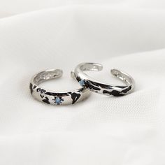 two silver rings sitting on top of a white cloth covered tablecloth, one with blue stones in the middle