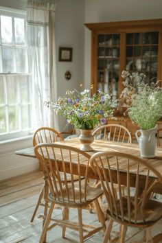 a dining room table with chairs and vases on it's centerpiece in front of a window