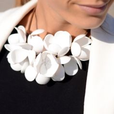 a woman wearing a white flower necklace on her neck and black shirt with a white blazer