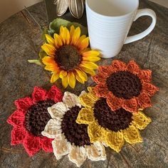 three crocheted sunflowers are next to a coffee cup