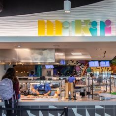 a woman standing in front of a food court with lots of counter space and artwork on the wall