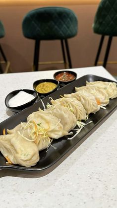 a black plate topped with dumplings and sauces on top of a white table