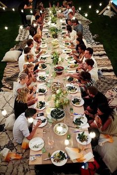 a group of people sitting at a long table with plates of food and lights on it