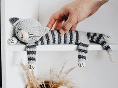 a crocheted cat sitting on top of a white shelf next to a plant