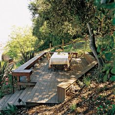 a wooden deck surrounded by lots of trees and bushes with benches on it in the woods