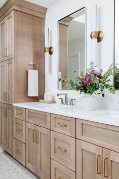 a bathroom with two sinks, mirrors and flowers in vases on the counter top