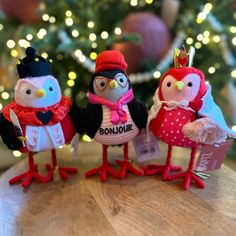 three small stuffed birds standing next to each other on top of a wooden table in front of a christmas tree