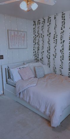 a white bed sitting in a bedroom next to a wall with vines on the walls