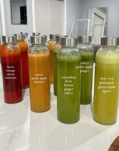 seven bottles with different types of liquid in them on a white countertop next to a mirror