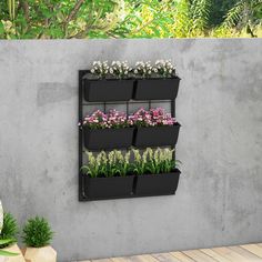 a wall mounted planter filled with flowers next to a cement wall and potted plants