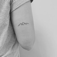 a small mountain tattoo on the left upper half of the arm, which is black and white