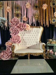 a white couch sitting in front of a wall with pink flowers and gold chains hanging from it